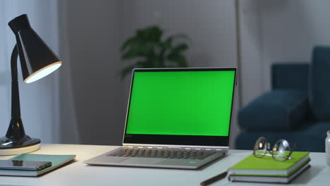 Laptop-Mit-Grünem-Bildschirm-Auf-Dem-Arbeitstisch-Im-Home-Office.-Mann-Schaltet-Tisch--Und-Stehlampen-Im-Wohnzimmer-Mit-Chroma-Key-Technologie-Ein.